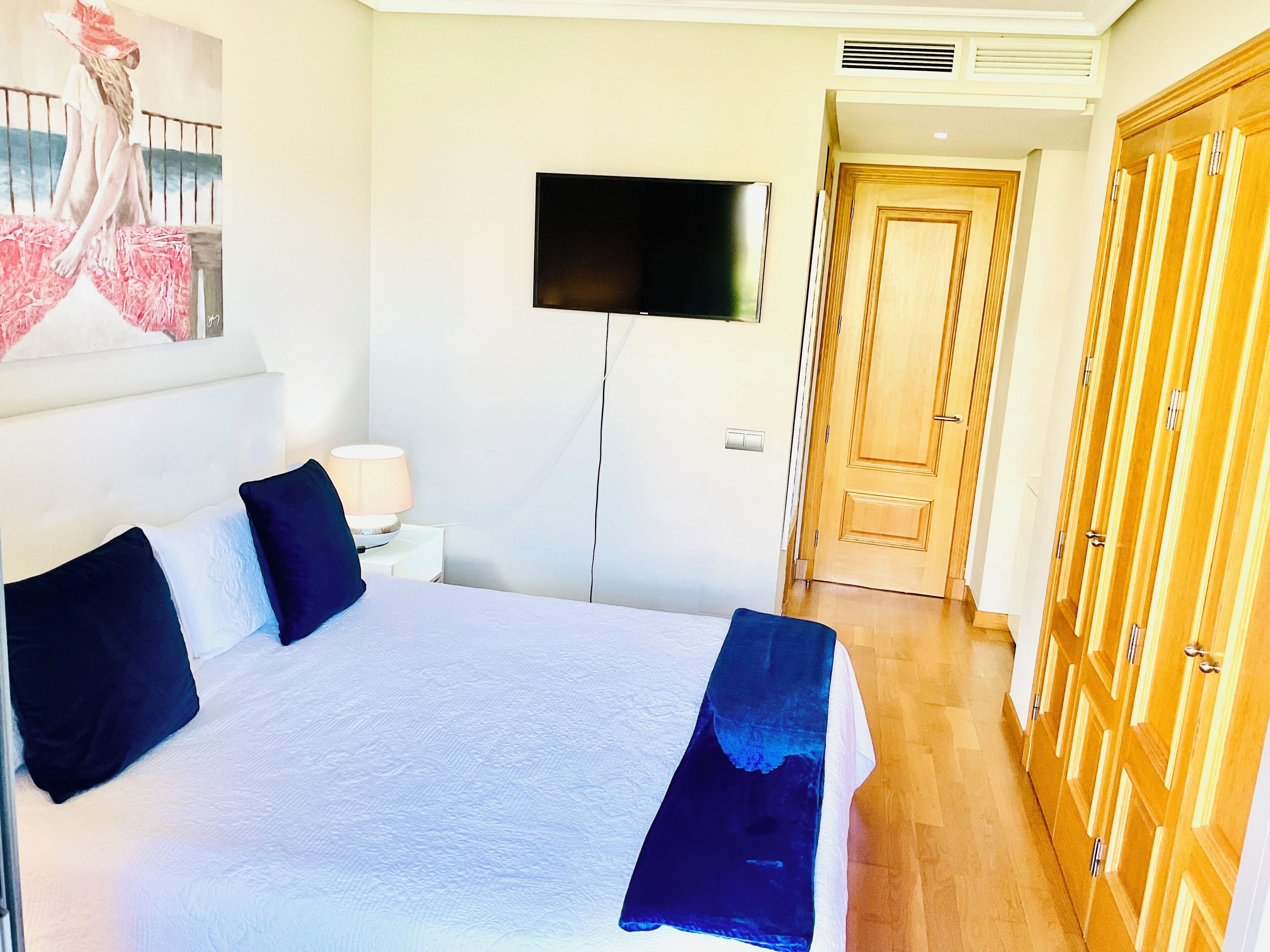 Ein Hotelzimmer mit Bett, Wandfernseher, Nachttisch mit Lampe und Holztüren.
