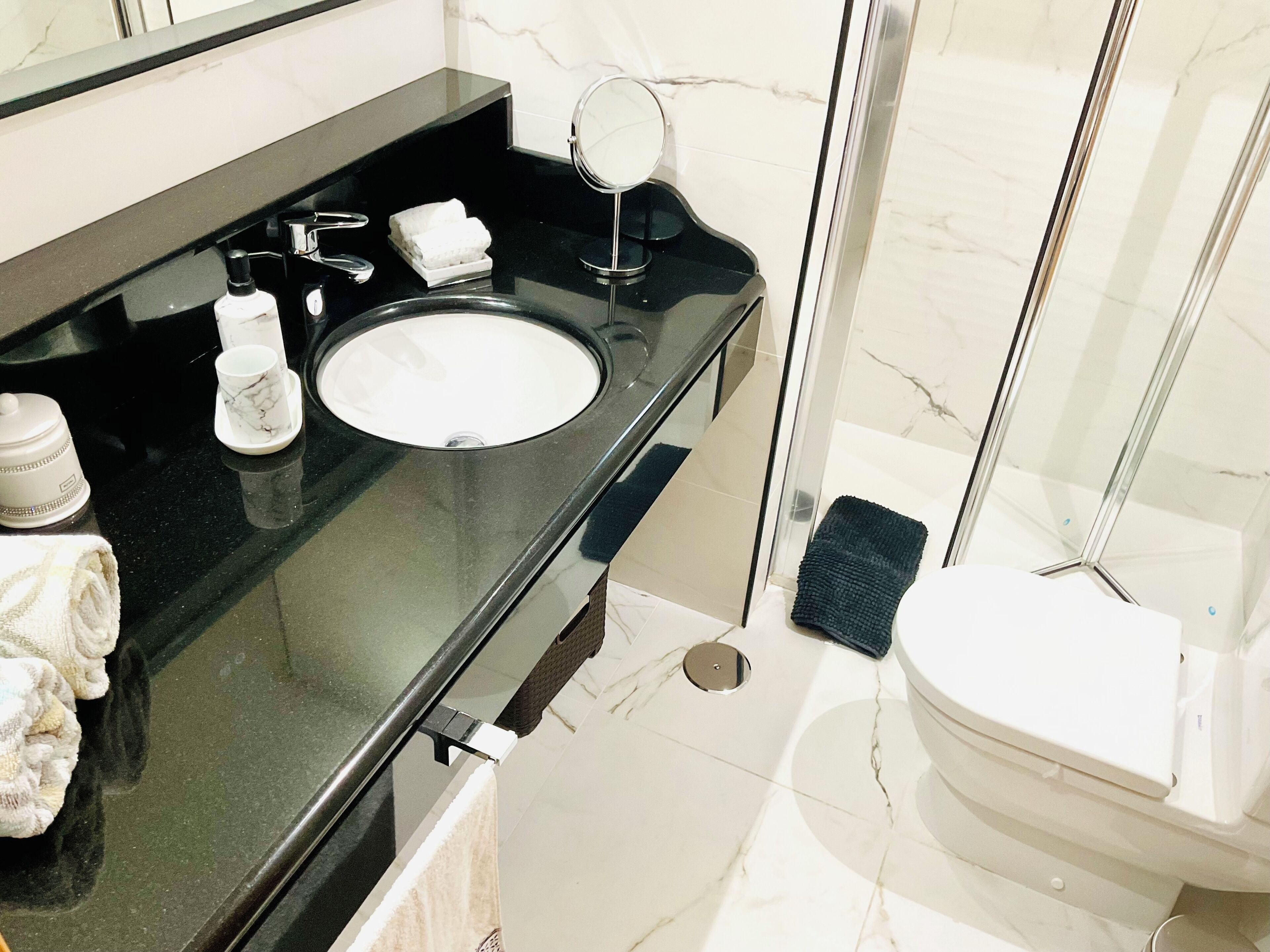 A modern bathroom with a black countertop, a white sink, a handheld showerhead, and a toilet.