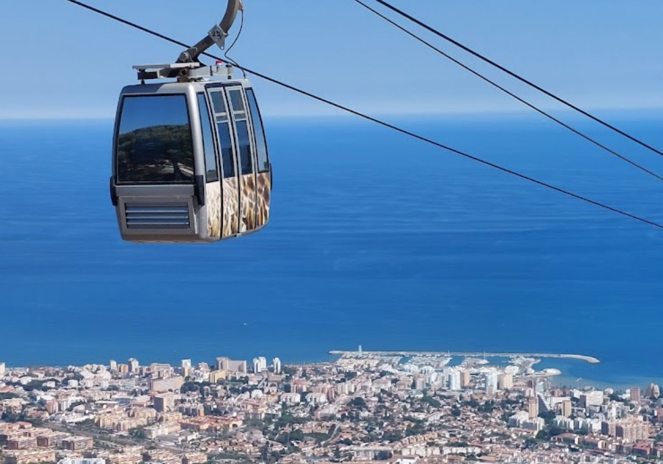 A cable car with a cityscape and coastline in the background.
