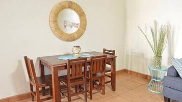 A dining area with a wooden table and chairs, a round mirror on the wall, and a small side table with a vase of plants.