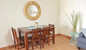 Ein Essbereich mit Holztisch und Stühlen, einem runden Spiegel an der Wand und einem kleinen Beistelltisch mit einer Pflanzvase.