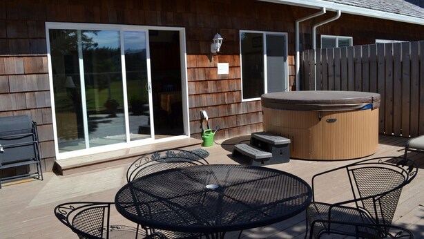 Eine Terrasse mit Whirlpool, Gartenmöbeln und einer Schiebetür, die zu einer überdachten Terrasse führt.