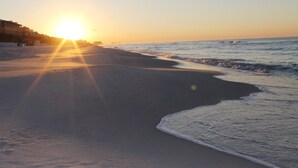 Een strand met de zon die ondergaat boven de oceaan, golven spoelen zachtjes op het strand.