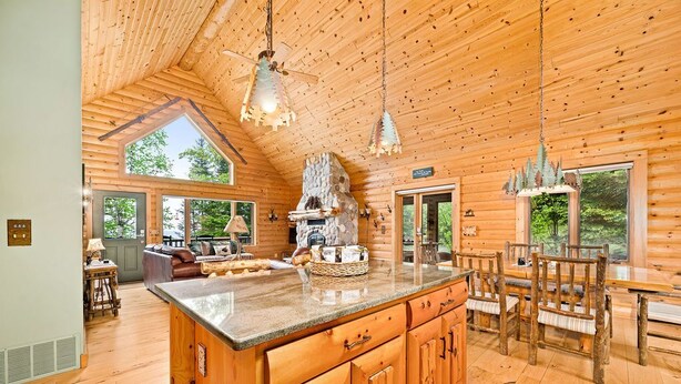 A log cabin interior with a large kitchen island, wooden dining table, and chairs.