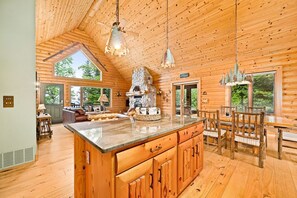 A log cabin interior with a large kitchen island, wooden dining table, and chairs. - Northwoods Luxury on Private Black Sand Beach (Two Harbors)