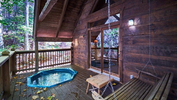 A wooden cabin with a deck, a hot tub, and a swing chair. - Cozy Rustic Hot Tub Cabin w/Hike in River Access - SWB (Sevierville)