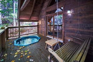 Een houten hut met terras, jacuzzi en schommelstoel.
