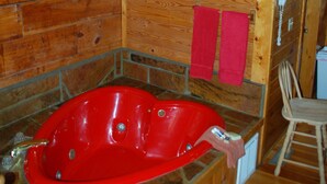 A wooden cabin interior with a red bathtub, wooden walls, a wooden ceiling, and a wooden chair. - Cozy Rustic Hot Tub Cabin w/Hike in River Access - SWB (Sevierville)