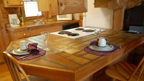 A kitchen with a wooden table set for two, equipped with a coffee maker, wine glass, and plates. - Cozy Rustic Hot Tub Cabin w/Hike in River Access - SWB (Sevierville)