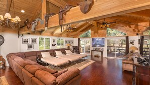 Un salón espacioso con un sofá grande marrón, un sofá más pequeño y una mesa de comedor. Varias ventanas ofrecen luz natural y vistas al exterior.