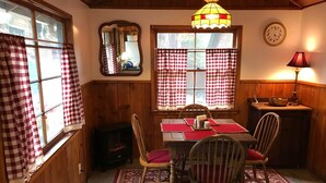 En mysig matplats med ett träbord, stolar, en matta och rutiga gardiner.