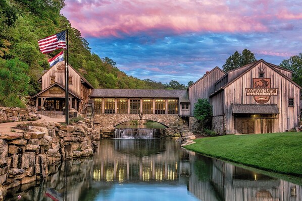 A rustic building with a sign reading "Dogwood Canyon Nature Park" and a stone bridge over a reflective water feature.