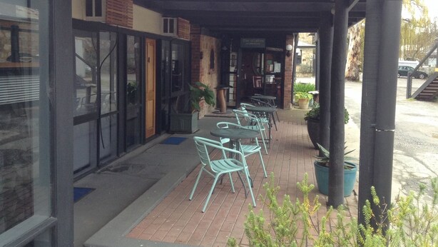 An outdoor seating area with tables and chairs, a covered walkway, and potted plants.