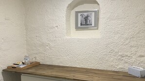 A small room with a white textured wall, a wooden counter, and a framed picture of a building.