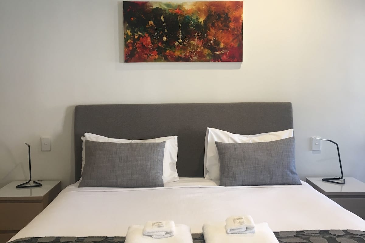 Habitación de hotel con una cama grande, dos almohadas, un cuadro en la pared y dos toallas sobre la cama.