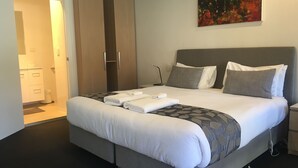 A modern hotel room with a large bed, grey bedding, a grey headboard, and a painting on the wall.