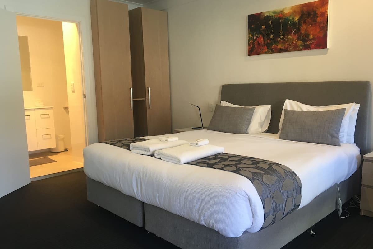 Habitación de hotel moderna con una cama grande, ropa de cama gris, cabecera gris y un cuadro en la pared.