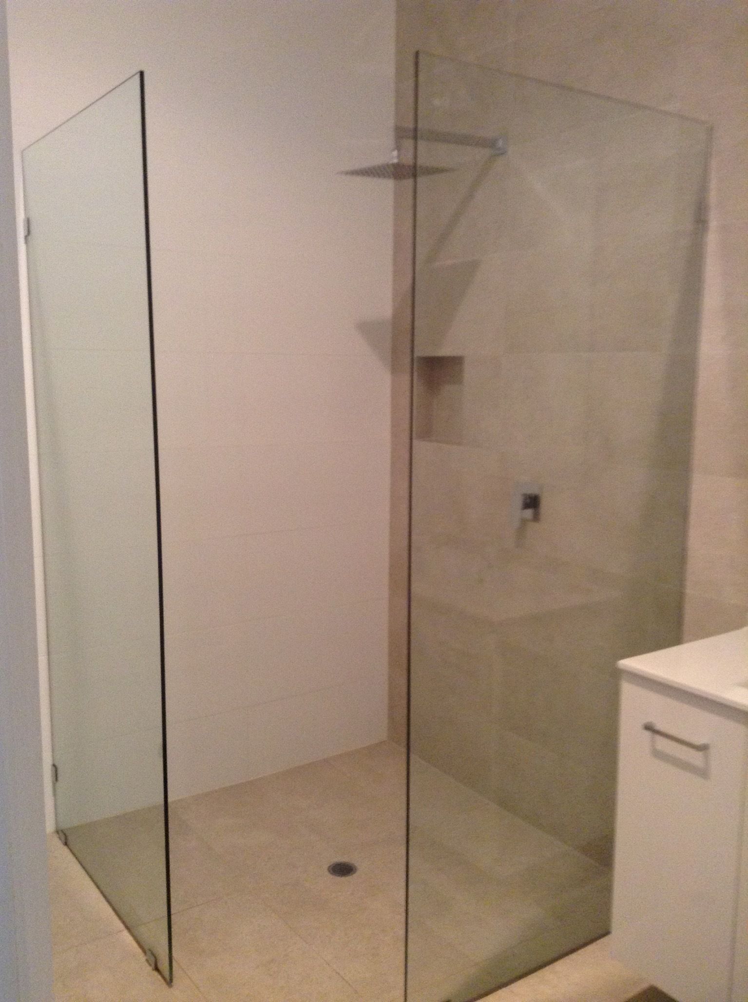 Una ducha con cerramiento de vidrio, suelo de azulejos y un armario blanco a la derecha.