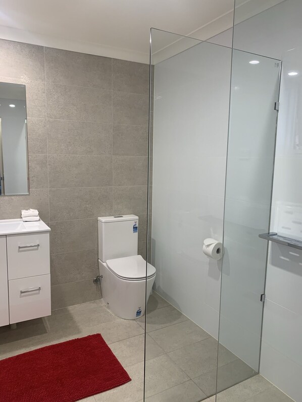 Un baño moderno con inodoro, cabina de ducha de vidrio y lavamanos blanco con alfombra roja.
