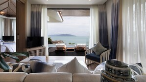 A modern living room with a large window overlooking a scenic view, a flat-screen TV, comfortable seating, and a wooden ceiling. - Cape Fahn Hotel – Private Islands Samui (Koh Samui)