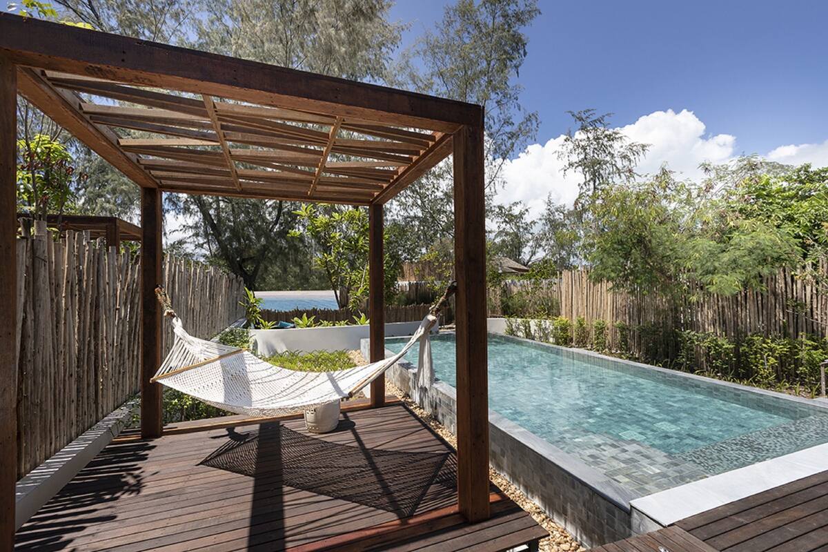 A wooden deck with a hammock, a swimming pool, and a wooden pergola.