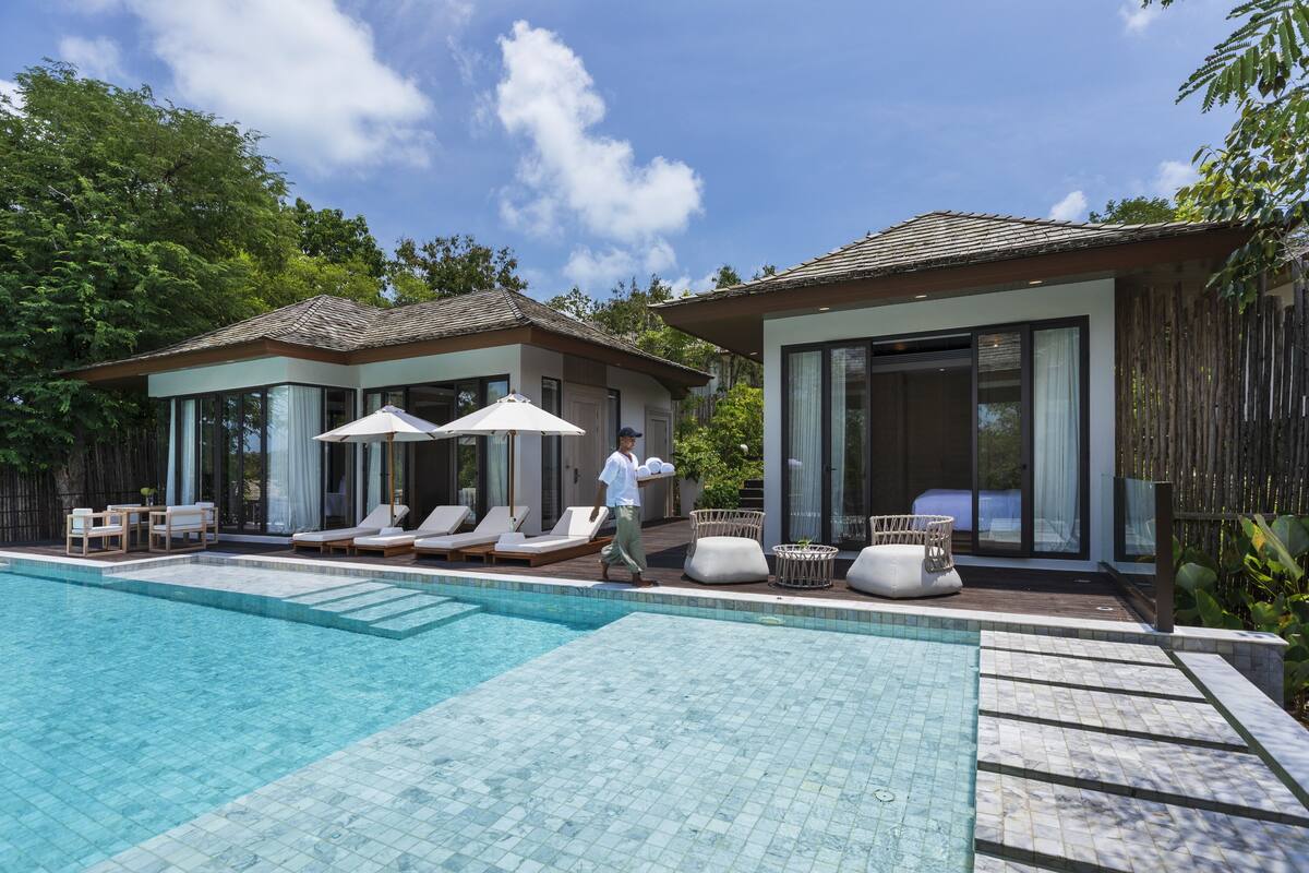 A modern pool area with lounge chairs and umbrellas, surrounded by wooden fences and lush greenery.