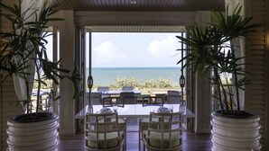 A covered outdoor dining area with a view of the ocean, featuring a table and chairs, and large potted plants. - Cape Fahn Hotel – Private Islands Samui (Koh Samui)