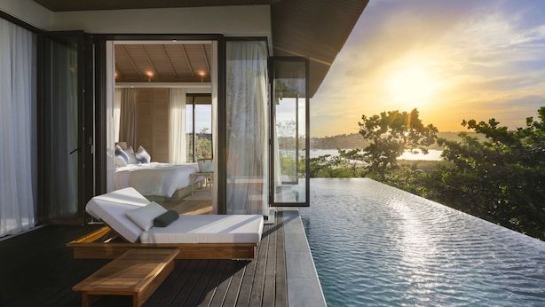 A modern infinity pool with a wooden deck and a bed with white linens. - Cape Fahn Hotel – Private Islands Samui (Koh Samui)