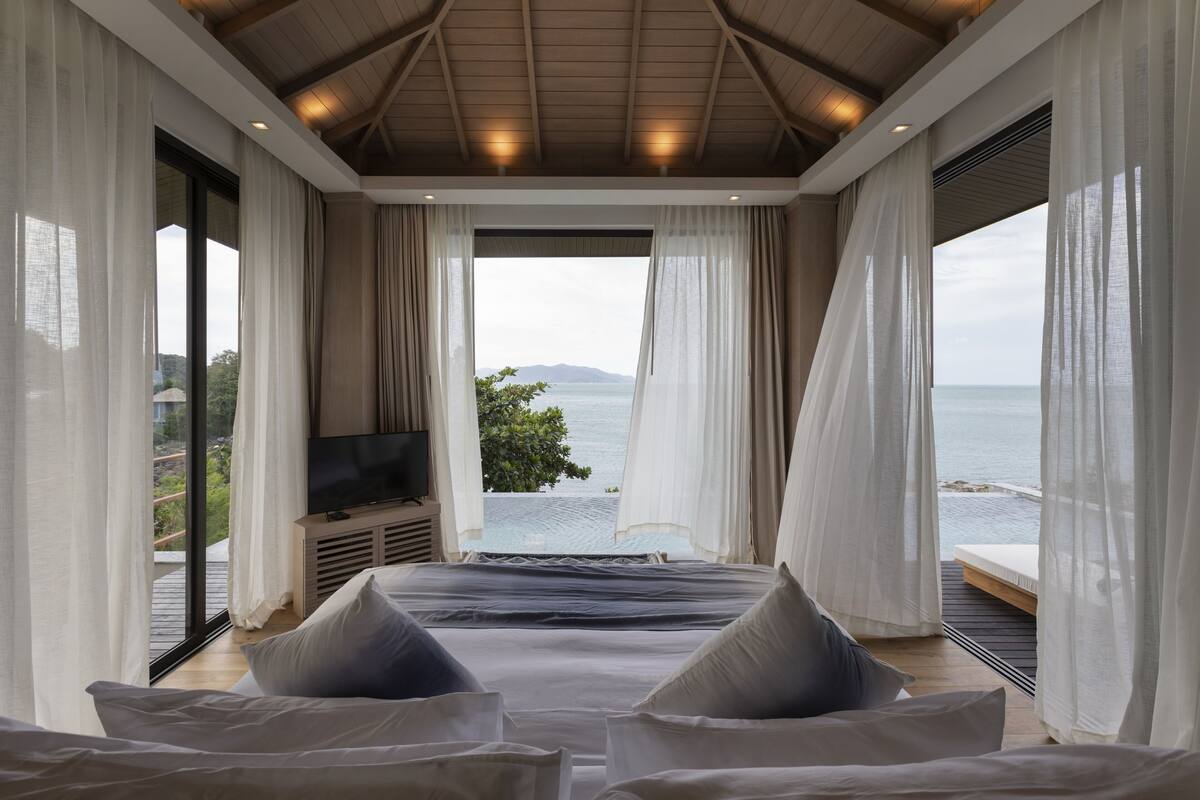 A bedroom with a large bed, a television, and a view of the sea.
