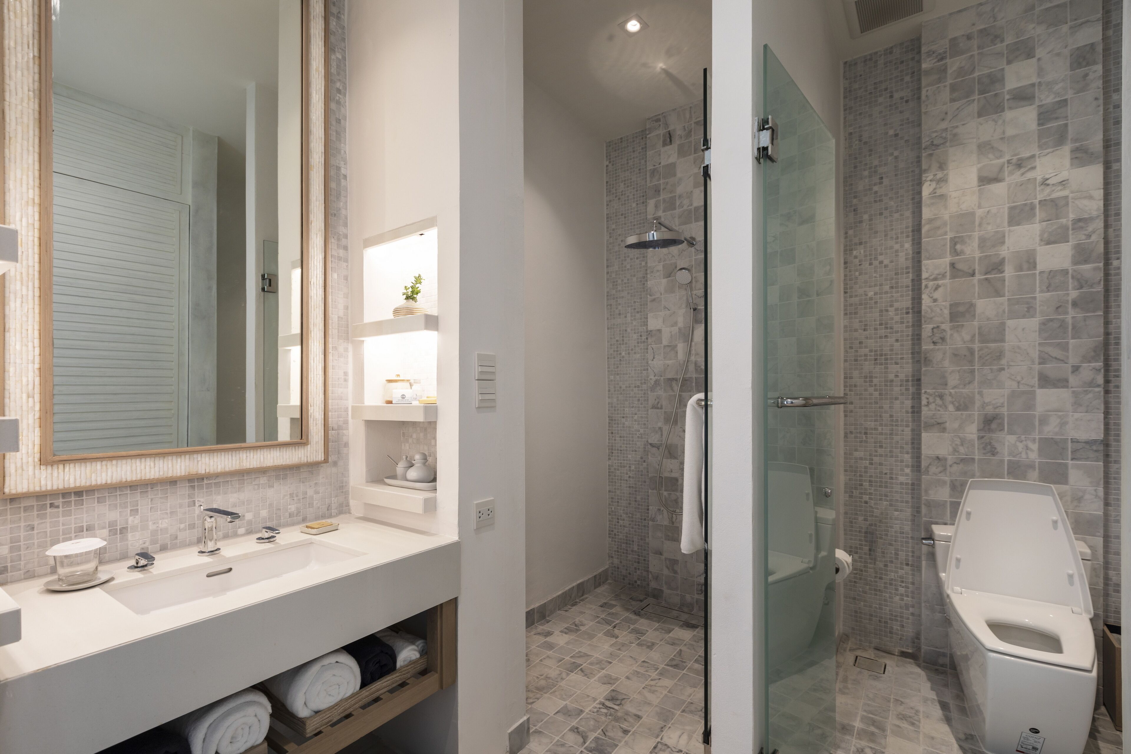 Un baño moderno con un espejo grande, ducha con mampara de vidrio y un inodoro.