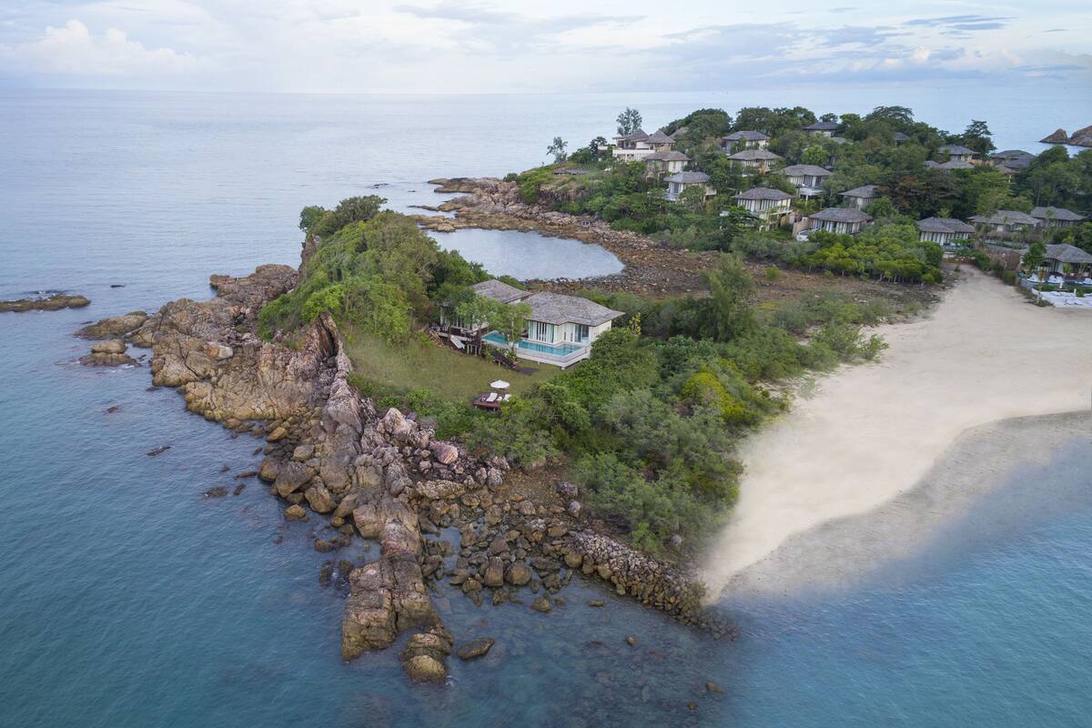 An aerial view of a coastal property with a private beach, rocky shoreline, and a cluster of houses.