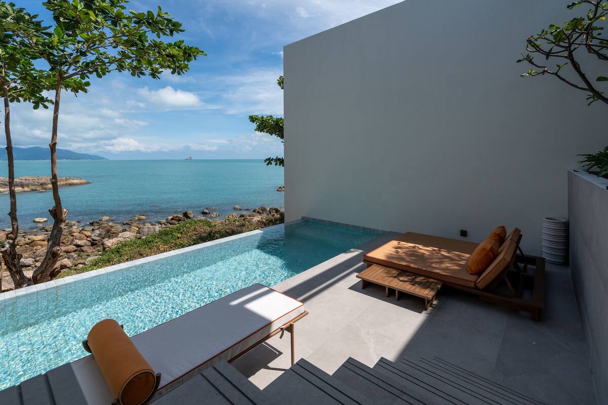 A modern outdoor pool area with a view of the sea, a lounge chair, and a small table.