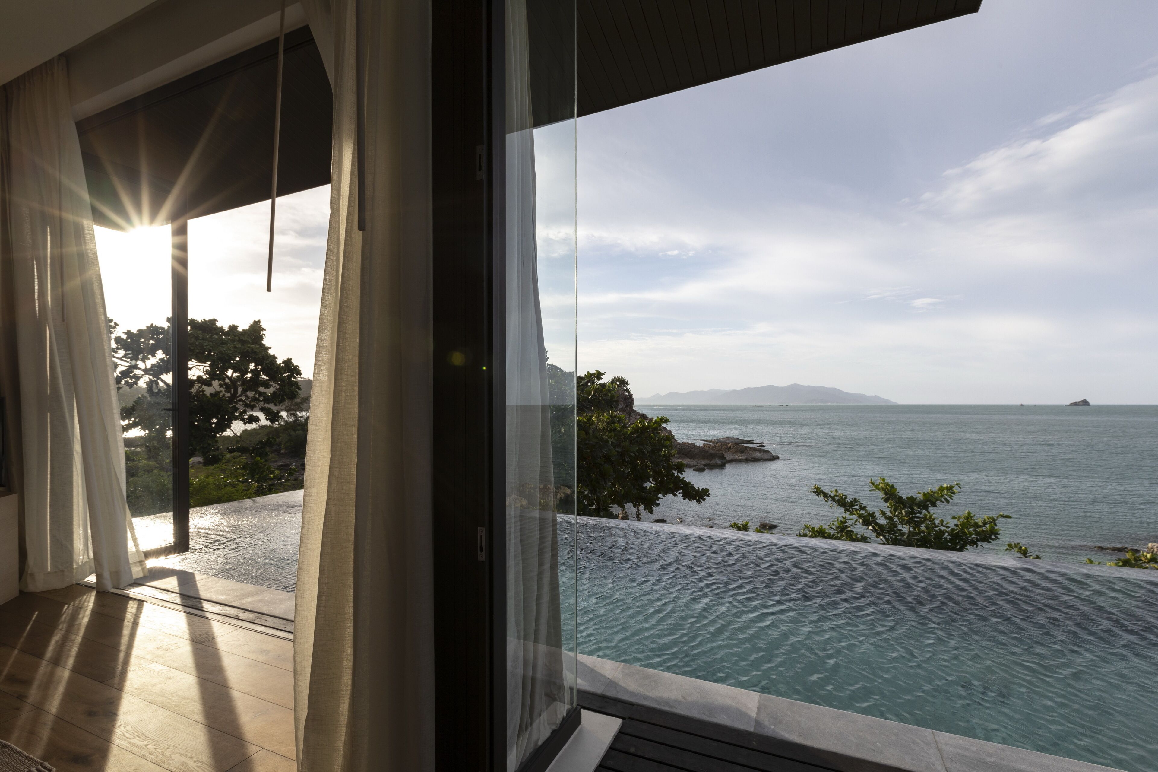 A modern room with a glass door leading to a balcony overlooking a pool and a coastal view.
