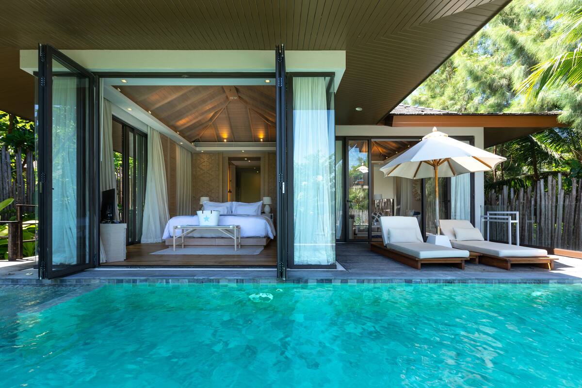 A modern resort with a swimming pool, a bedroom with a balcony, and a lounge area with sun loungers.