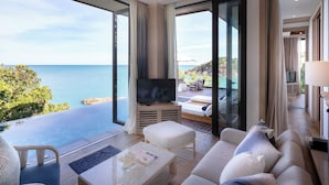 A modern living room with a large TV, a sofa, and a coffee table. There is a balcony with a view of the ocean. - Cape Fahn Hotel – Private Islands Samui (Koh Samui)