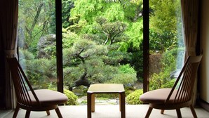 Dos sillas de madera y una pequeña mesa frente a una ventana con vista a un jardín exuberante.