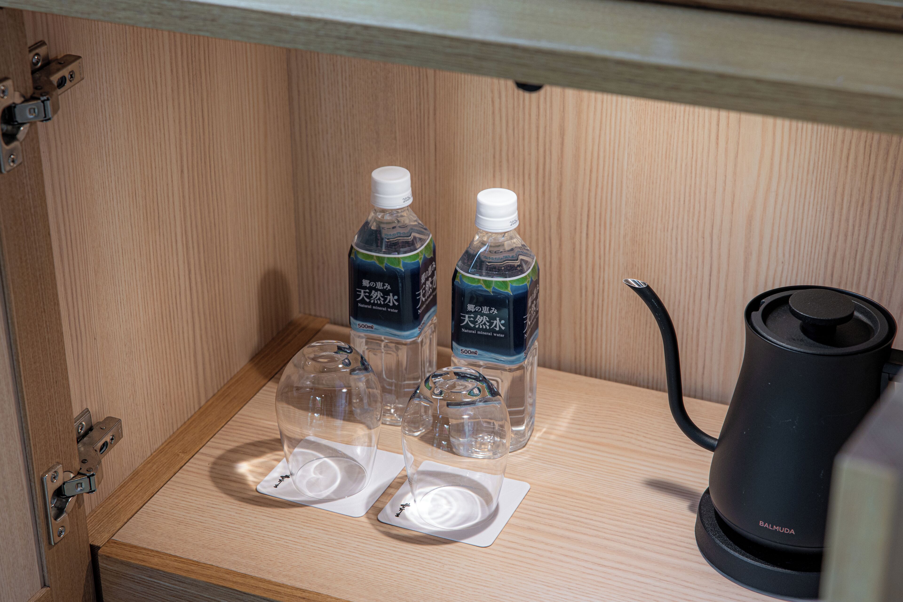 Een houten kastje met twee waterflessen, twee glazen en een zwarte elektrische waterkoker.