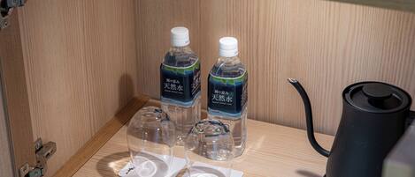 Een houten kastje met twee waterflessen, twee glazen en een zwarte elektrische waterkoker.