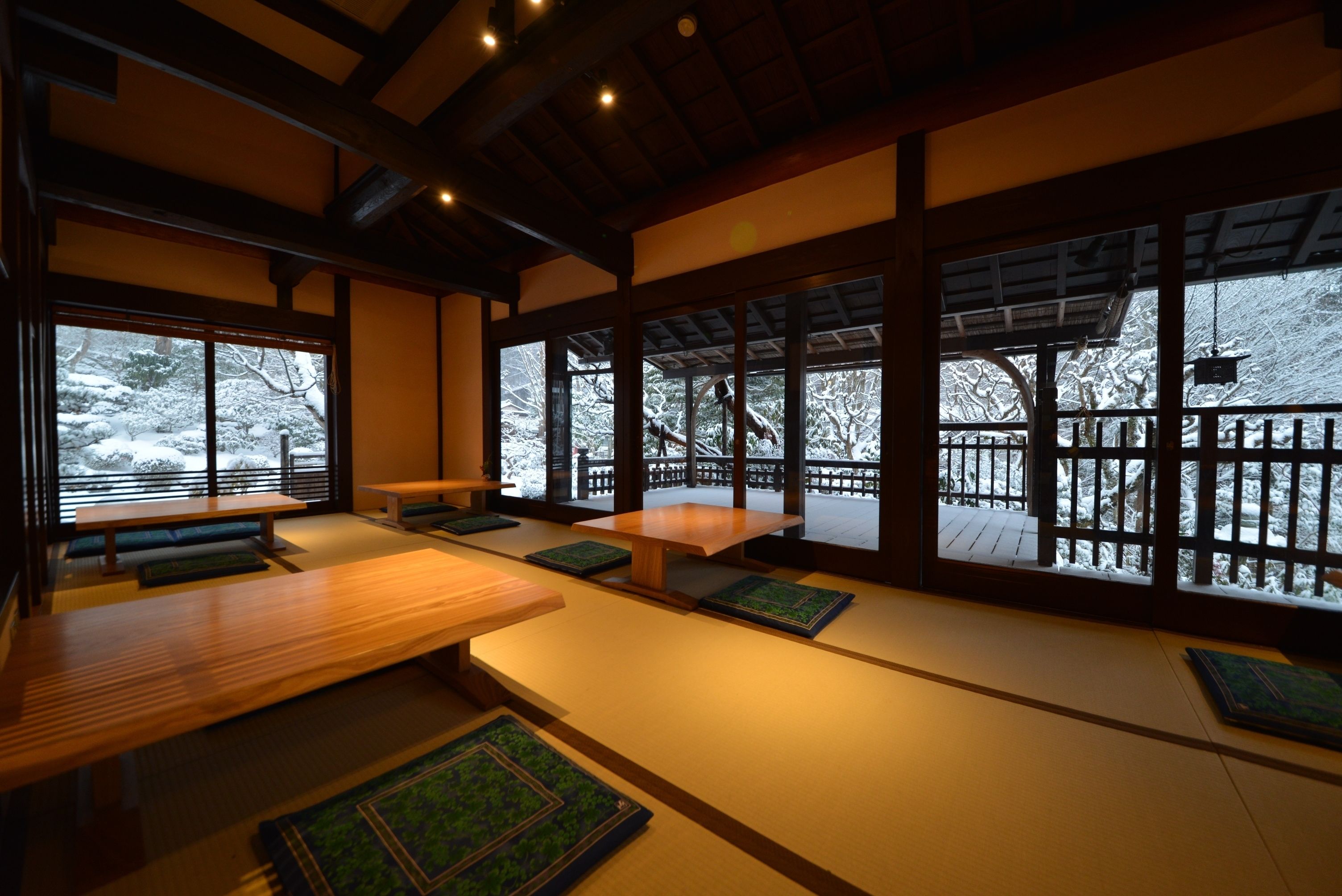 Ein traditioneller japanischer Raum mit Tatami-Boden, Holzbänken und großen Fenstern mit Blick auf einen verschneiten Garten.