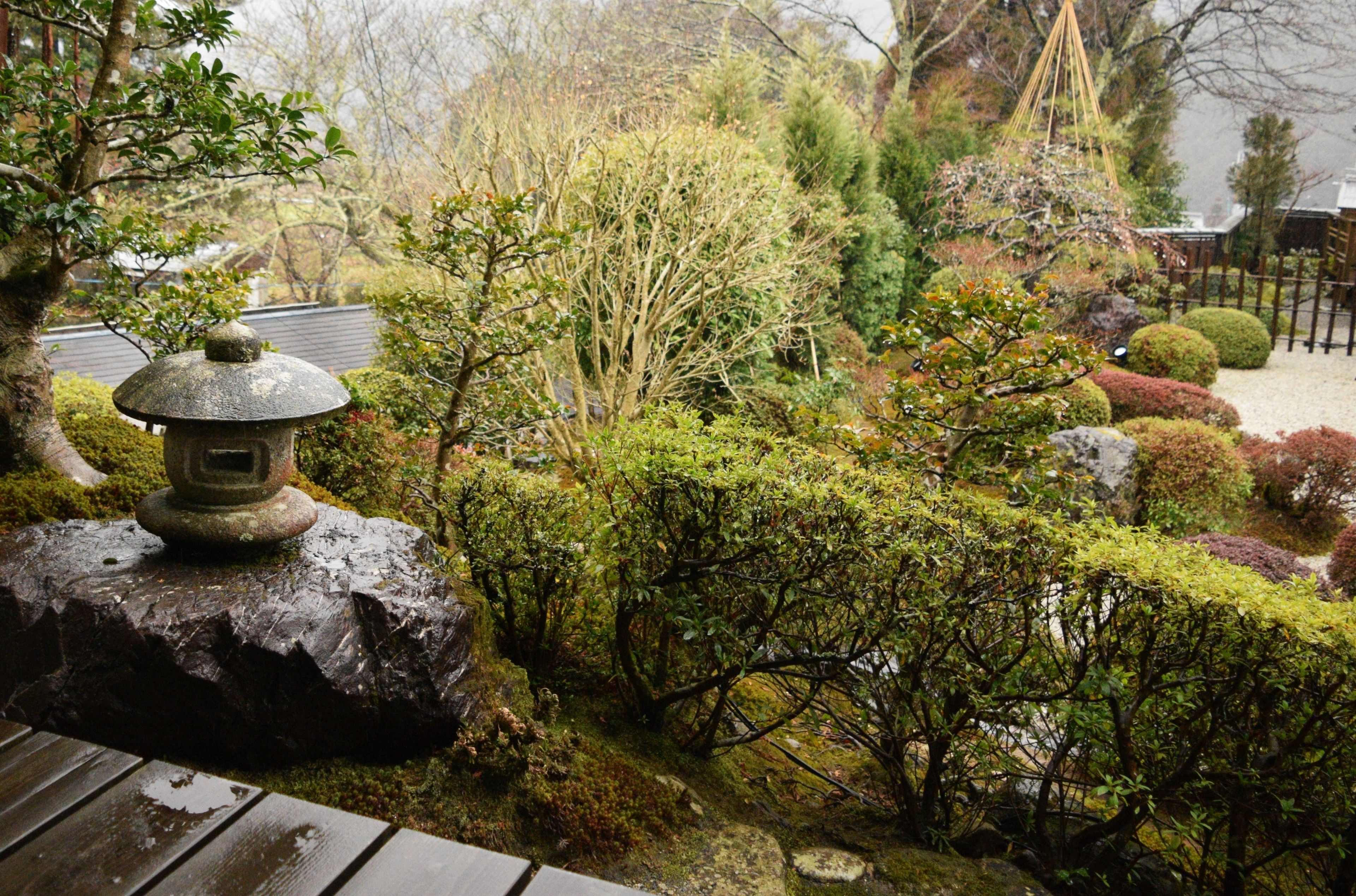 Un jardín japonés tradicional con un farol de piedra, arbustos cuidadosamente podados y un banco de madera.
