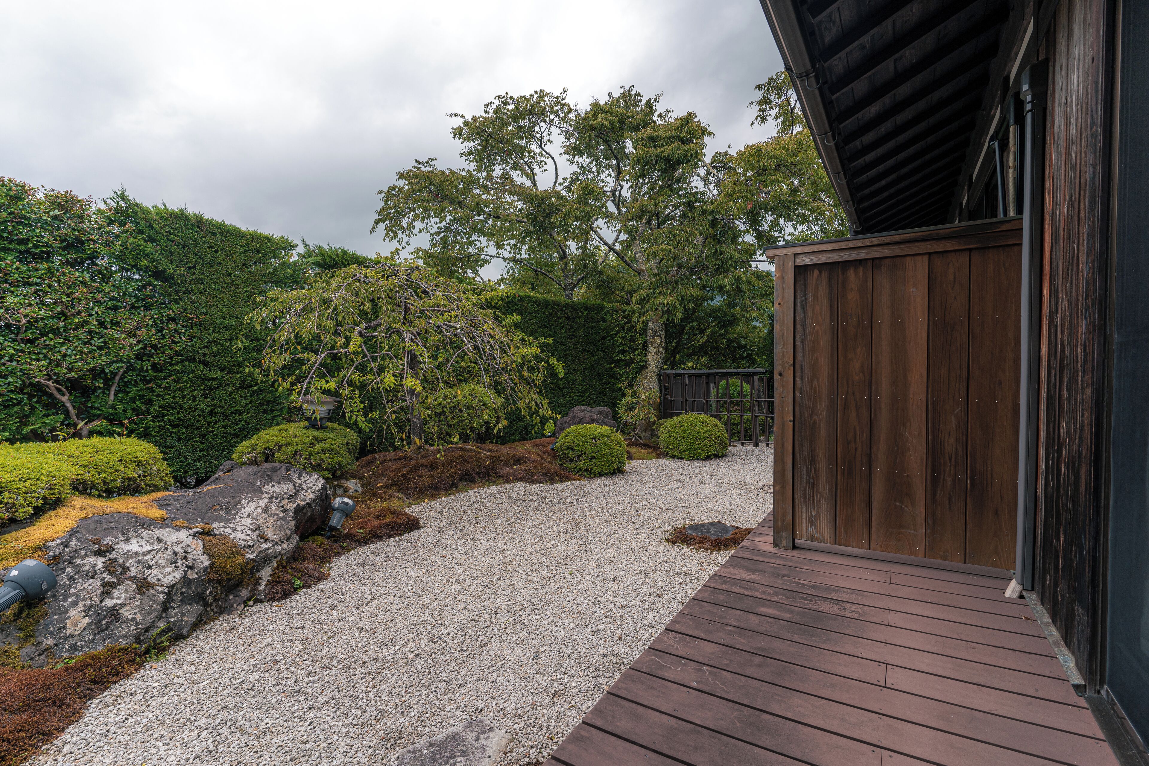A wooden deck leading to a traditional Japanese building with a gravel path and landscaped garden.