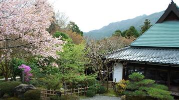 A traditional Japanese building with a green roof, surrounded by a well-maintained garden with cherry blossoms and various shrubs.