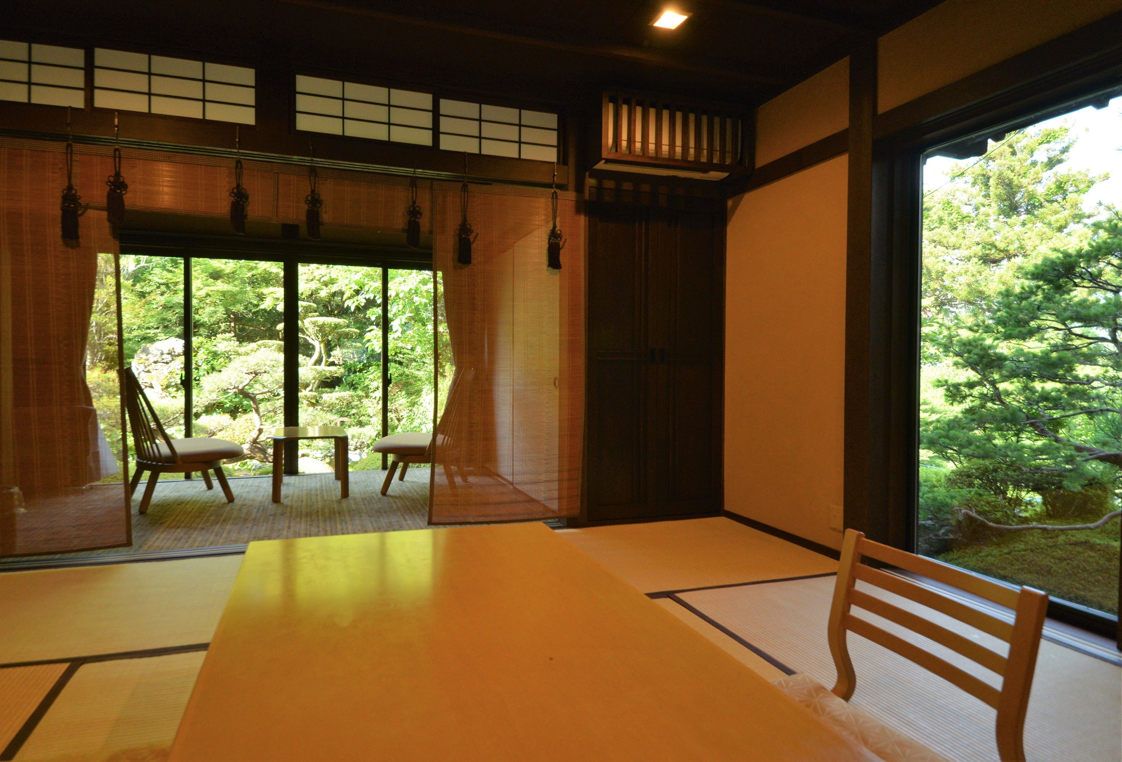 A traditional Japanese room with tatami flooring, a low table, and a view of a lush garden.