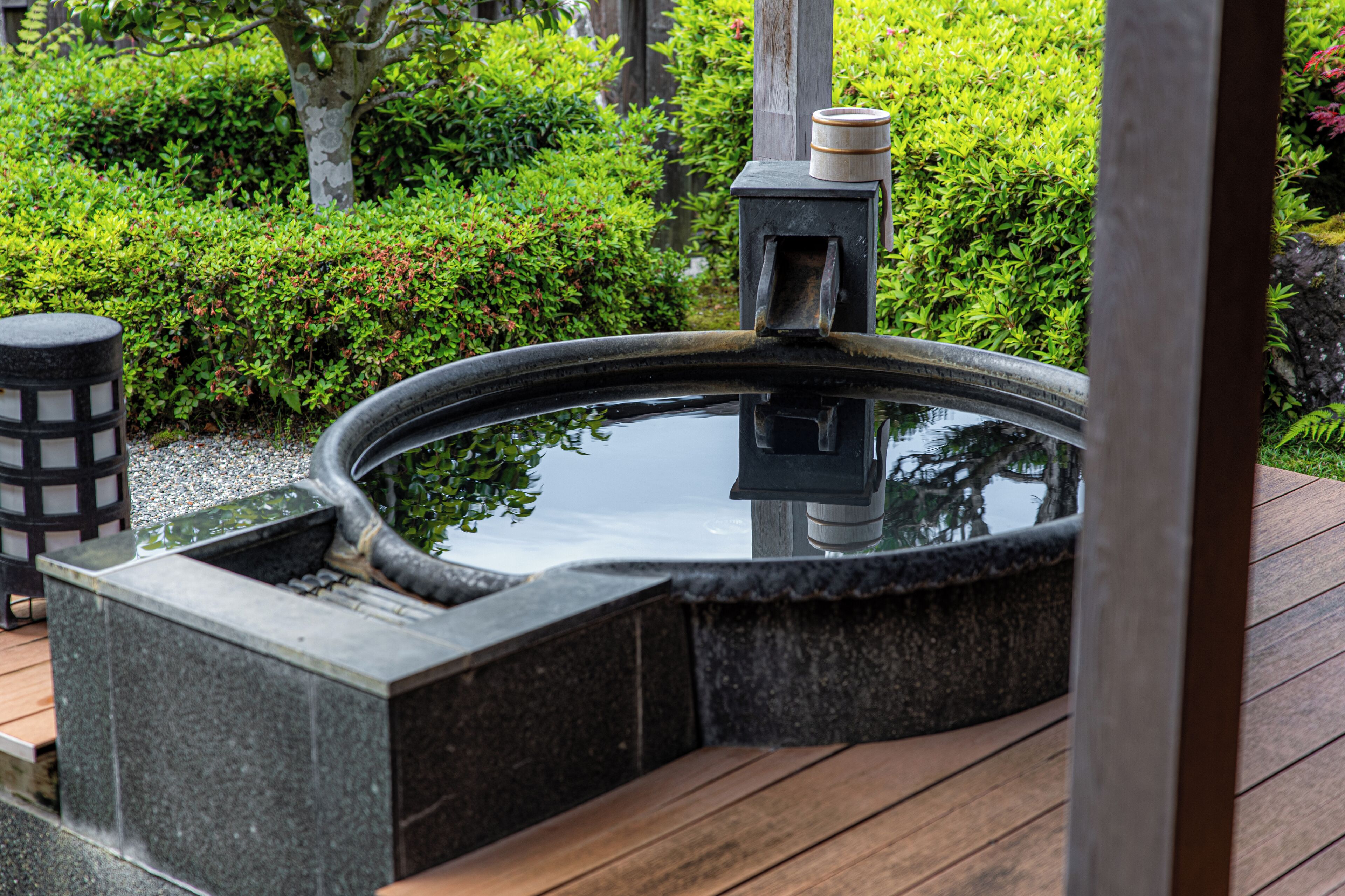 A stone hot tub with a wooden deck and a lantern.