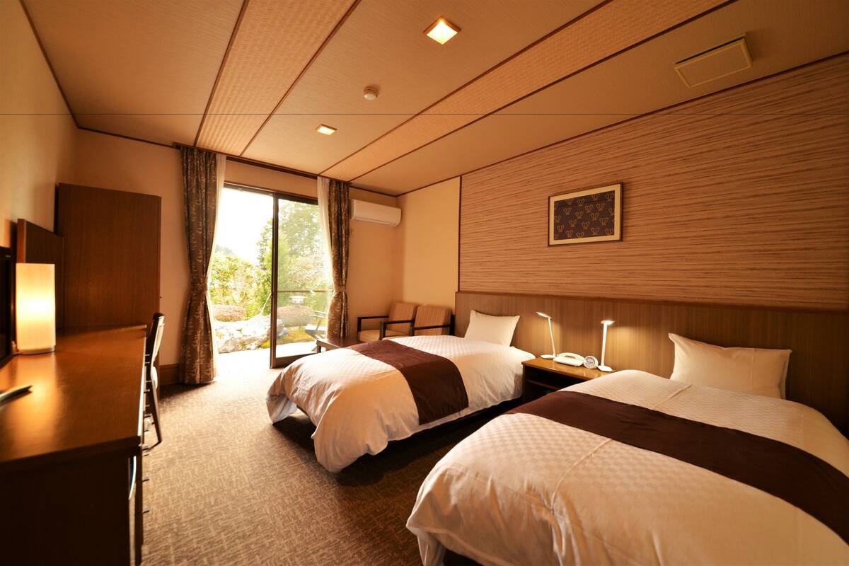 A hotel room with two beds, a desk, and a window with curtains.