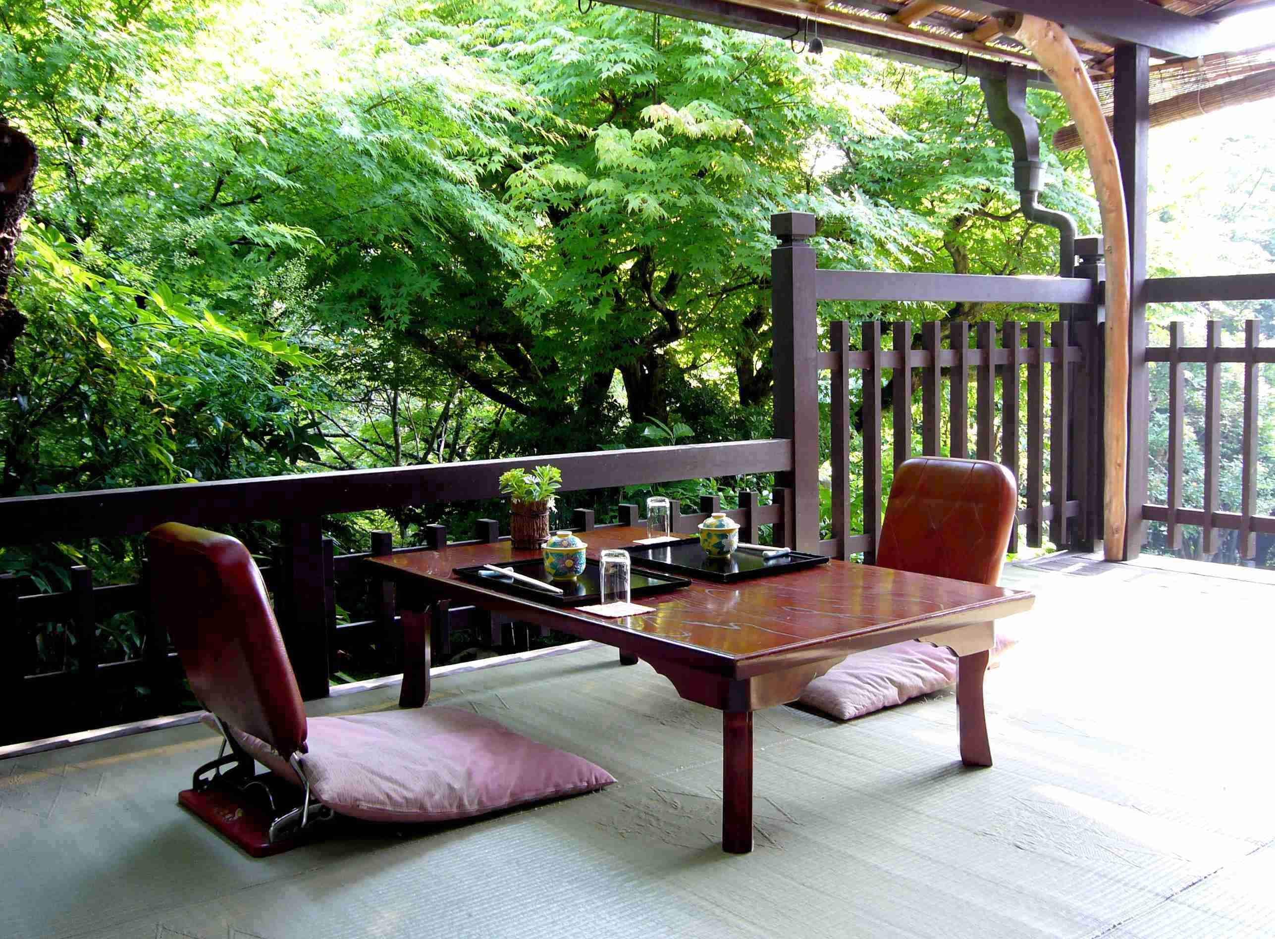Un terrazzo in legno con tatami, un tavolo con un vaso e un vassoio, e due sedie con cuscini.