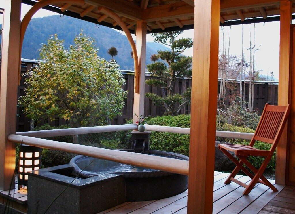 Una terraza de madera con un tinaco de hidromasaje de piedra, una silla de madera y vistas a la montaña.