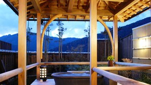 Una terraza de madera con un jacuzzi, barandillas de madera y vistas a montañas.