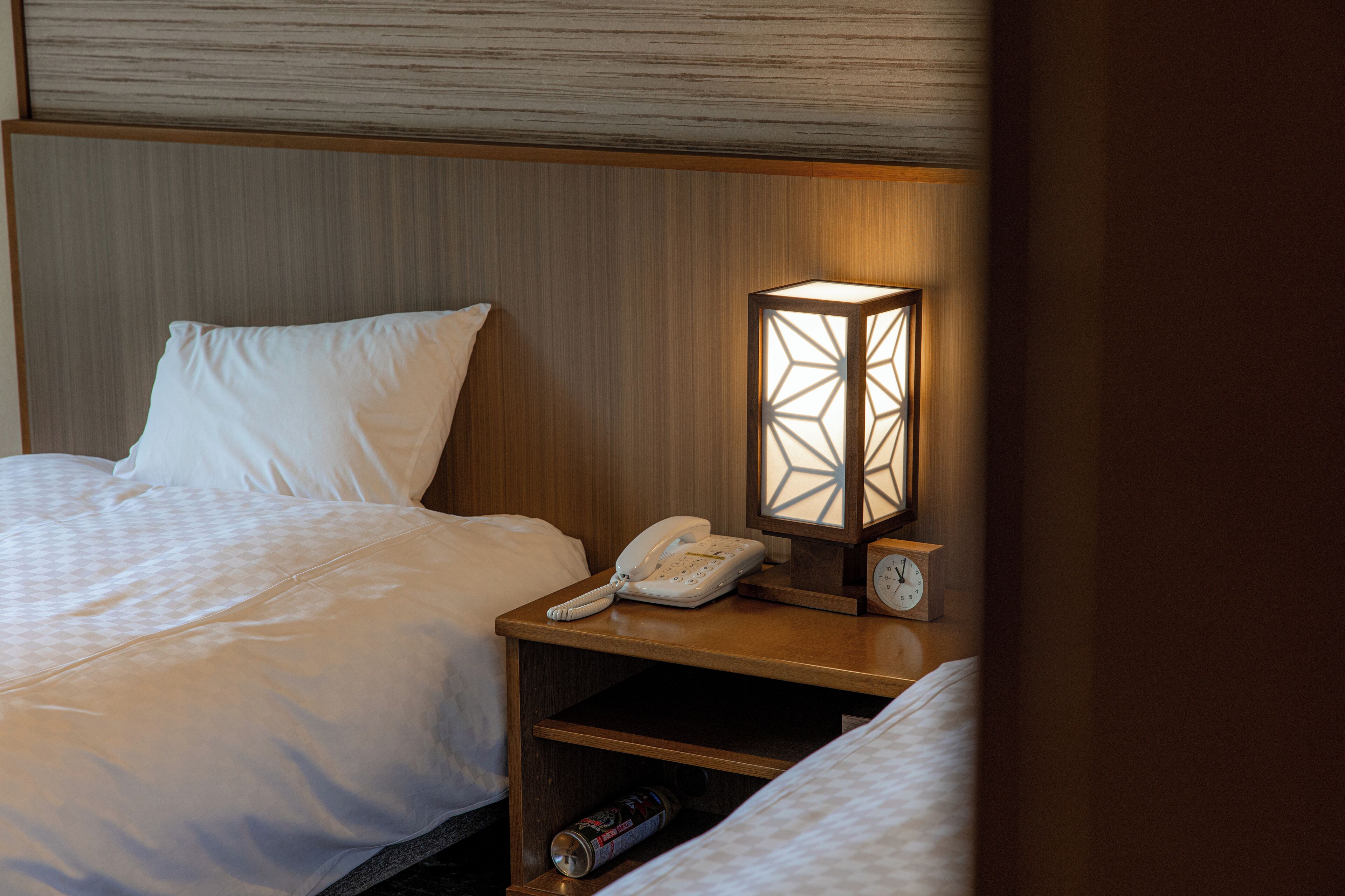 A hotel room with a bed, a bedside table with a lamp, a phone, and a clock.