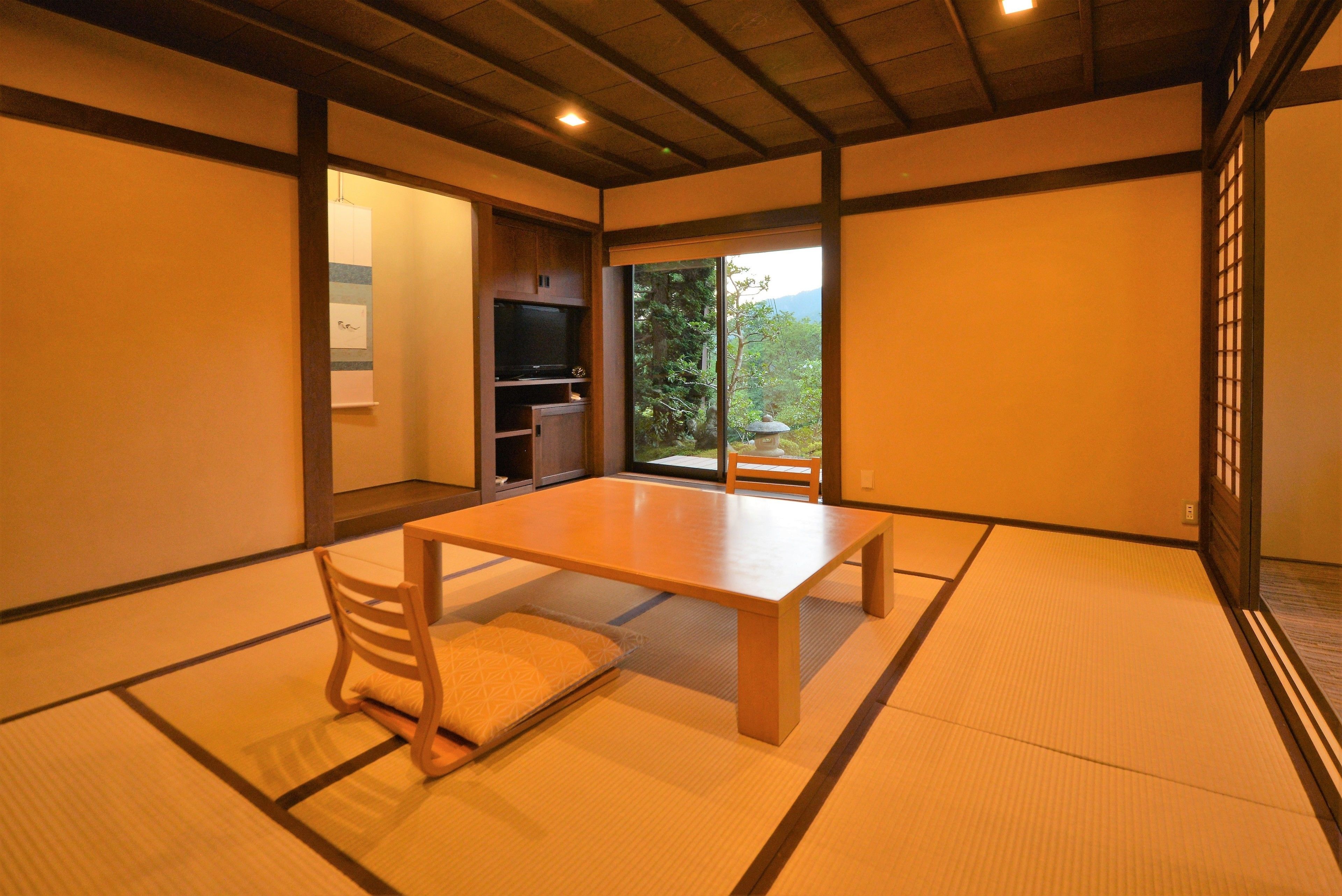 A traditional Japanese room with tatami flooring, a low table, and a sliding door leading to a balcony with a view of greenery.